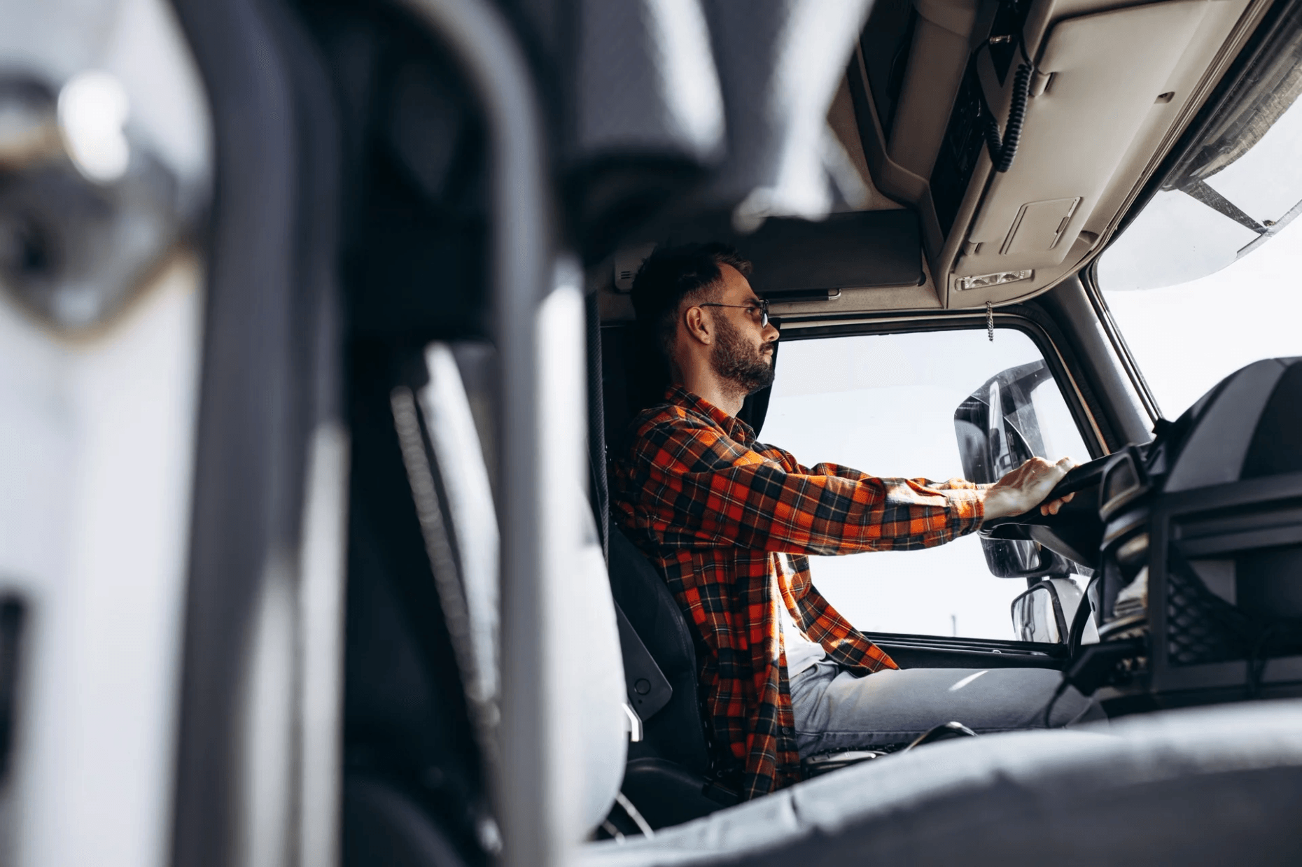 Truck driver seated at the wheel inside the cab of a heavy-duty vehicle.