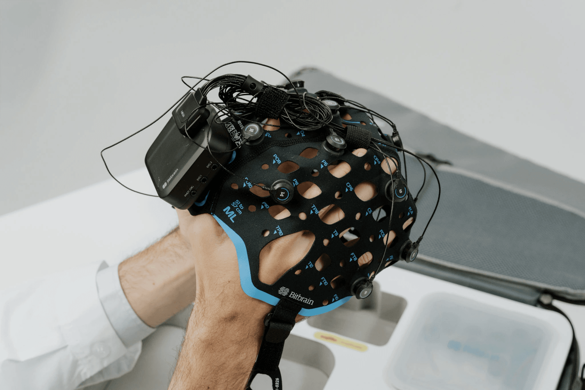 Close-up of hands holding a Bitbrain EEG cap with the integrated recording device and visible wiring.