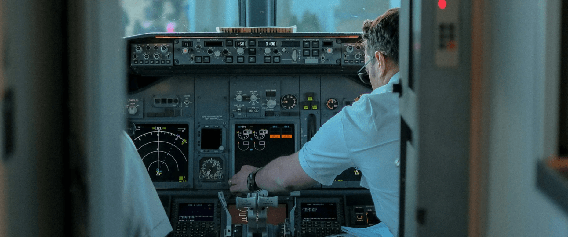 Person operating the controls in a commercial aircraft cockpit surrounded by flight instruments and control panels.