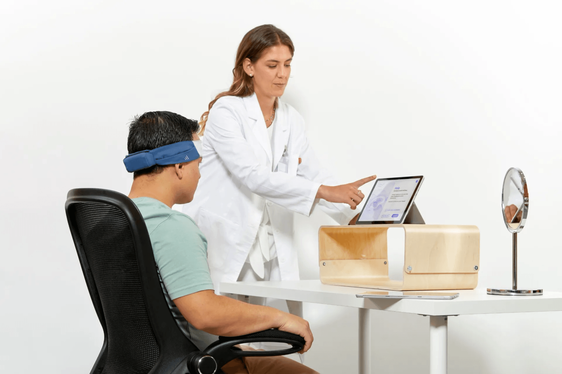 Participant wearing the Bitbrain Ikon textile EEG system during a neurofeedback session while a researcher points to the results displayed on a screen.